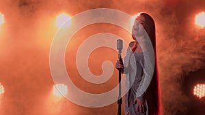 Sexy glamorous female singer performs on stage in a long evening dress. A woman sings a song into a vintage microphone