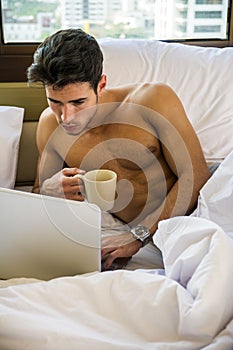 handsome young man in bed with coffee or tea cup