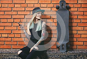 hipster girl in tattoo against a red brick wall with a long board.