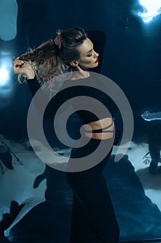 Sexy lady in black dress posing in studio on dark foil background