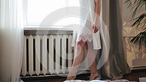 Sexy legs and feet of young beautiful bride in white peignoir walk across floor of the room and turn around 180 degrees
