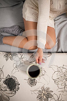 Sexy legs of shapely girl. She is holding a cup of hot coffee.