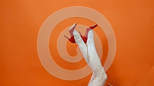 Sexy long legs on high heels red shoes and white fishnet stockings on orange background. Retro style