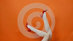 Sexy long legs on high heels red shoes and white fishnet stockings on orange background. Retro style