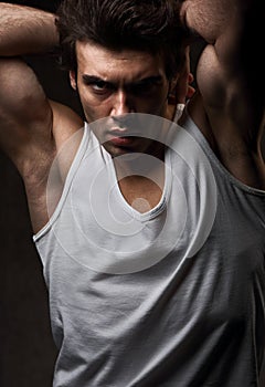 Sexy male model posing in white underwear in dark shadow background with angry emotional look. Closeup portrait