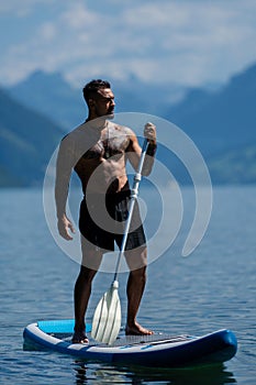 Sexy man with paddle board. Man paddling on paddleboard. Muscular strong Hispanic man on sup board paddle surfing. SUP