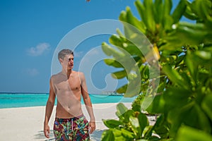 Sexy man in swimming shorts standing at the beach at the tropical island