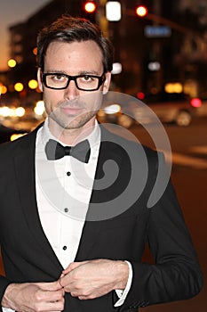 man in tuxedo and bow tie posing in the city streets at night