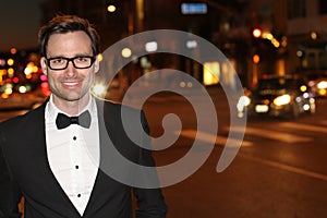 man in tuxedo and bow tie posing in the city streets at night