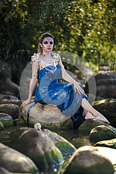 Sexy Mermaid of Sea in Artistic Caucasian Blond Woman With Strasses on Face Sitting in Blue Wet Dress on Rocky Shore Outdoor