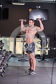 Sexy muscular man doing shoulders exercise and looking at the mirror