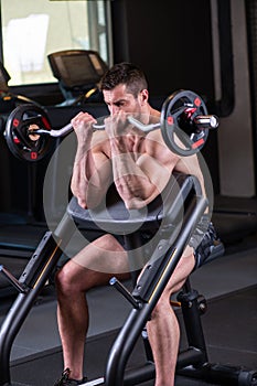 Sexy muscular man sitting on the bench and doind biceps exercise