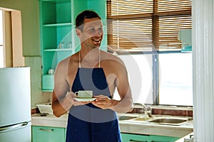 Sexy muscular topless man in apron making coffee for breakfast in kitchen.