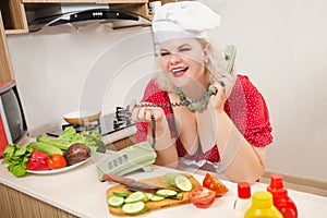 Sexy pinup plus size caucasian woman in cook`s hat talking by phone and making salad and healthy food on the kitchen