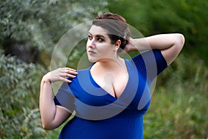 Sexy plus size fashion model in blue dress with a deep neckline outdoors, beautiful fat woman with big breasts in nature