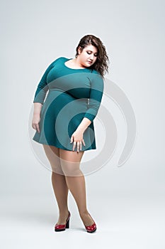 Sexy plus size fashion model in green dress, fat woman on gray background, body positive concept