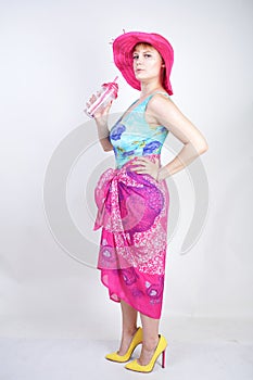 Sexy plus size girl in a blue swimsuit, fuchsia hat with brim and in a trendy bright pareo stands on a white background in the Stu