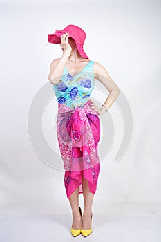 Sexy plus size girl in a blue swimsuit, fuchsia hat with brim and in a trendy bright pareo stands on a white background in the Stu