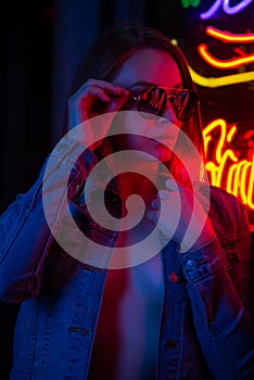 Sexy portrait of a young girl with an open bust in sunglasses and with in the night city, with creative light on the background of