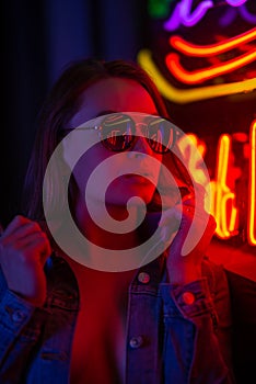 Sexy portrait of a young girl with an open bust in sunglasses and with in the night city, with creative light on the background of