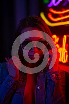 Sexy portrait of a young girl with an open bust in sunglasses and with in the night city, with creative light on the background of