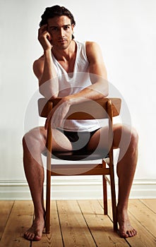 Sexy, portrait of young man on chair by white wall with underwear for strong, body building and hot muscles. Serious