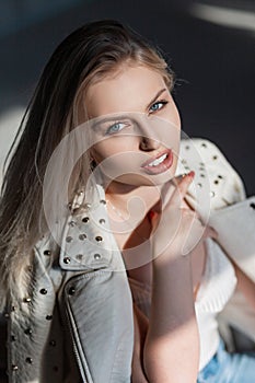 Sexy pretty attractive young blond woman with natural make-up in a stylish jacket with metal rivets in a room on a sunny day.