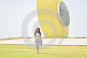 Sexy, pretty young woman on gray dress, fashion sunglasses and blue jeans stand on the grass the background of a falling UFO plate