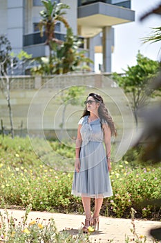Sexy, pretty young woman on gray dress, fashion sunglasses and blue jeans stand on the grass the background of a green park, looks