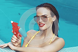 Sexy retro woman shooting with water gun in swimming pool