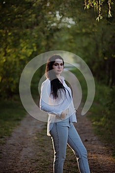 Sexy sensual brunette walks in a summer forest at sunset in a white blouse and jeans