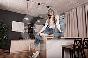 Sexy slim red-haired young woman in a stylish white top in fashionable blue jeans in trendy leather sneakers is resting on a