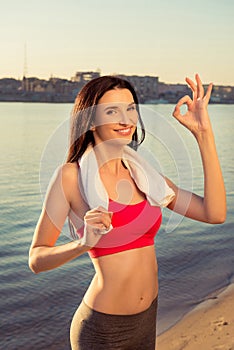Sexy slim woman posing with towel gesturing `OK` on the seaside