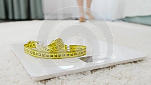 Sexy slim woman weighting on scales and walking on soft carpet in bedroom. Concept of dieting, loosing weight and