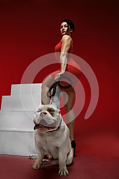 Sexy and srong brunette woman posing with bully dog in studio on red background. Rear view