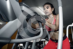 and sweaty Asian woman training hard at gym using elliptical pedaling machine gear in intense workout