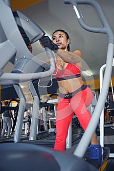 and sweaty Asian woman training hard at gym using elliptical pedaling machine gear in intense workout