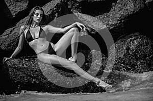 Sexy tanned girl in bikini swimsuit on sea background. Fashion woman in bikini relax on beach. sexy woman on rocks stone
