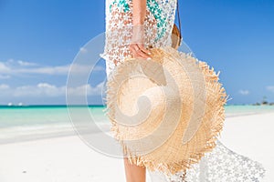 Sexy tanned girl in blue bikini and white tunica holding big straw hat on the seashore. Concept vacation, travel