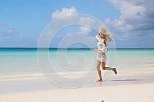 Sexy tanned girl in blue bikini and white tunica running on the seashore. Beautiful model sunbathes and rests on sea. Concept