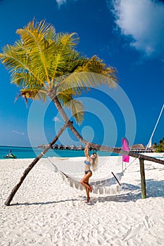 Sexy tanned woman bikini model at Maldives tropical sand beach. Glamour girl in swimsuit on hammock in paradise. Perfect body