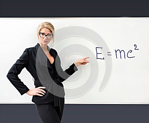 Sexy teacher in a black suit near the blackboard in a modern classroom shows the formula of physics. Copy space