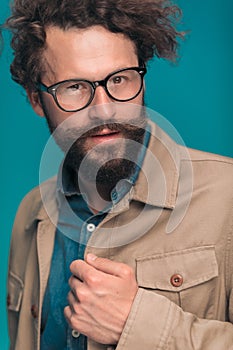 Sexy unshaved man with beard and moustache arranging beige jacket