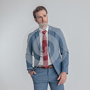 Sexy unshaved man in blue suit holding hand in pocket and looking to side