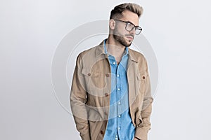 Sexy unshaved man in denim shirt with glasses holding hands in pockets