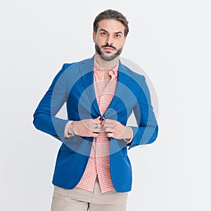 sexy unshaved man looking forward while buttoning blue jacket