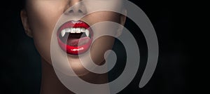 Sexy Vampire Woman`s red bloody lips close-up. Vampire girl licking fangs with tongue. Fashion Glamour Halloween art design