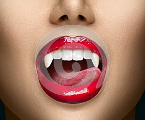 Sexy Vampire Woman`s red bloody lips close-up. Vampire girl licking fangs with tongue. Fashion Glamour Halloween