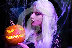 Sexy witch with hallowen makeup and long white hair holding pumpkin on black background