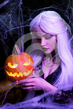 Sexy witch with hallowen makeup and long white hair holding pumpkin on black background
